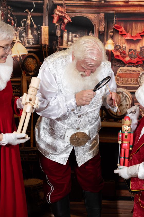Santa Doug examining a nutcracker with a magnifying glass in the toy workshop