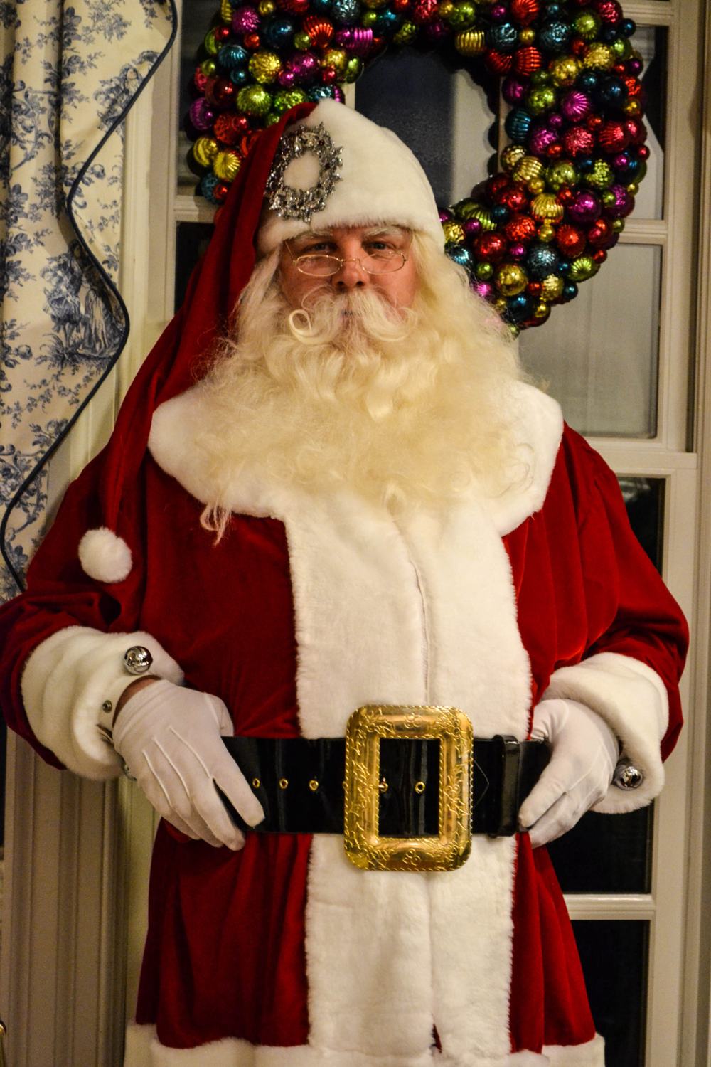 Santa Doug in a red and cream coat beneath a large wreath